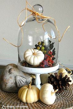 a glass clochel filled with pumpkins and gourds on top of a table