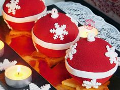 three red cakes decorated with white snowflakes are on a table next to candles