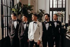 a group of men in tuxedos standing next to each other near a window