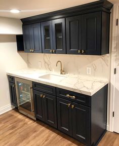 an empty kitchen with black cabinets and marble counter tops, wood floors, and white walls