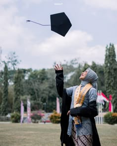 a woman wearing a hijab is flying a kite in the air with her hands