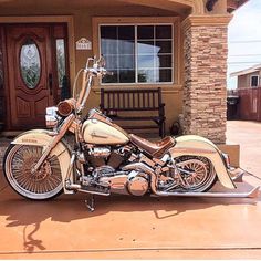 a tan motorcycle parked in front of a house next to a wooden door and bench