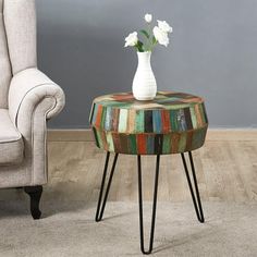 a vase with flowers sitting on top of a multicolored table next to a chair