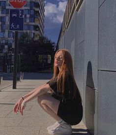 a young woman sitting on the ground next to a wall with a stop sign in the background