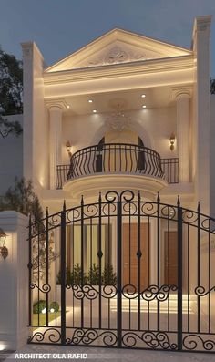 a large white house with an iron gate and stairs leading to the front door at night