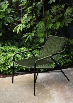 a green lawn chair sitting on top of a cement floor next to trees and bushes