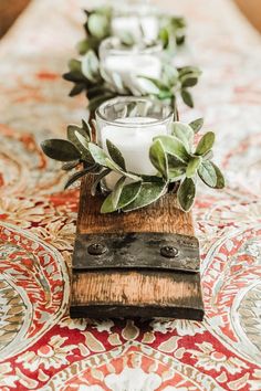 candles are lined up on a wooden block with greenery and leaves in them, along with other decorative items