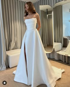 a woman in a white wedding dress standing next to a mirror with her hand on her hip