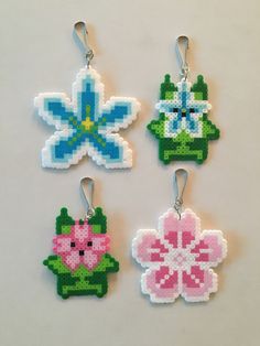 four cross stitch flower ornament hangings on a white surface with two pink and one blue flowers