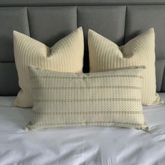 two pillows on top of a bed with white sheets and grey headboard behind them