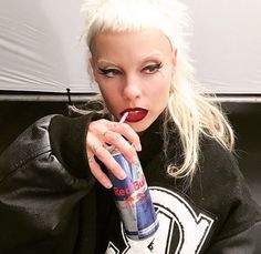 a woman with white hair and makeup holding a bottle in her hand while sitting on a couch