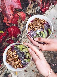 two hands holding bowls filled with fruit and nuts