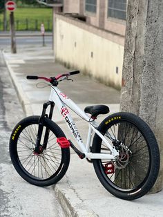 a white and red bike parked next to a tree on the side of a road