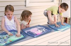 three young children are painting on paper outside