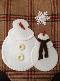 two felt snowmen sitting next to each other on top of a plaid table cloth