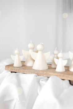 several white candles are placed on a wooden tray in the shape of angel's