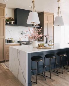 a kitchen island with stools next to it and lights hanging from the ceiling above