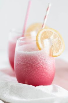 two glasses filled with pink and yellow liquid next to each other on a white cloth