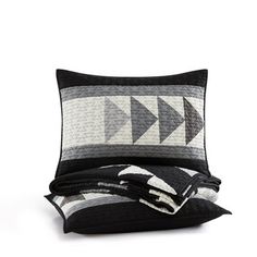 a black and white quilted pillow with two pillows on the bottom, one has an arrow