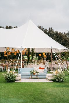 an outdoor tent set up with couches, tables and chairs for a wedding reception