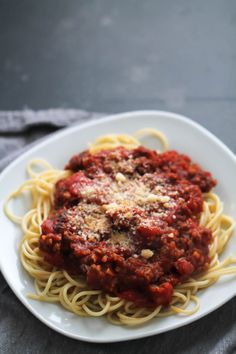 spaghetti with sauce and parmesan cheese on a white plate, ready to be eaten