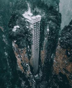 an aerial view of a tall building surrounded by mountains and trees in the middle of winter