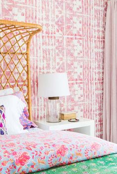 a bedroom with pink and green wallpaper, white bedding and a rattan headboard