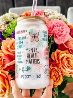 a person holding up a cup with flowers in the background and an inscription on it that says mental health matters