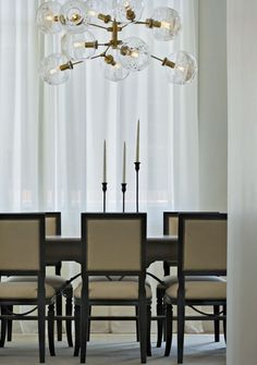 a chandelier hanging over a dining room table with chairs and candles in front of it