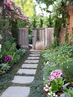 a garden path with stepping stones leading to a wooden fence and flowers in the foreground