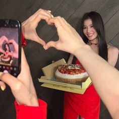 a woman taking a photo with her cell phone while holding a cake in front of her