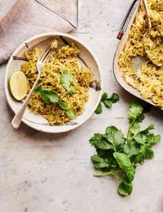 two bowls filled with yellow rice and garnished with cilantro, parsley and lime