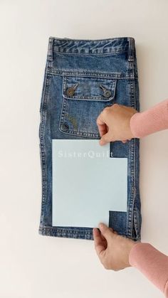 two hands holding a piece of paper in front of a pair of jeans