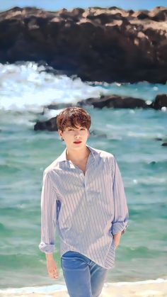 a boy is walking on the beach near the water