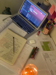 an open laptop computer sitting on top of a desk next to a notebook and pen