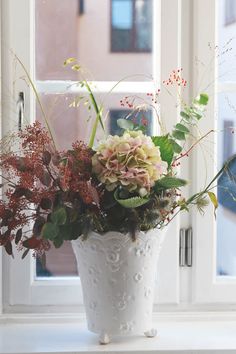 a white vase filled with lots of flowers on top of a window sill