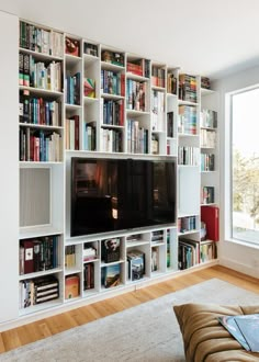 a living room filled with lots of books and a flat screen tv mounted on a wall