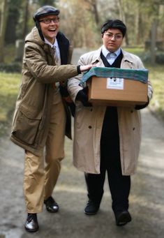 two men in coats and hats are carrying a box on a path through the woods