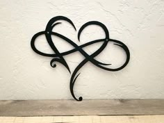 a metal heart with an intricate design on the side of a white wall next to a wooden table