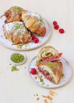 two plates filled with pastries and raspberries on top of a wooden table