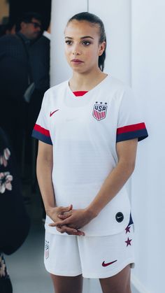 a woman standing in front of a wall wearing a white shirt and shorts with the usa flag on it