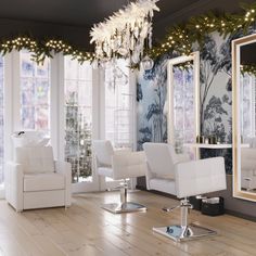 a salon with white chairs and chandelier in front of large windows that have christmas lights on them