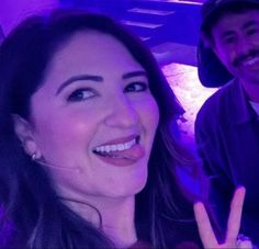 a man and woman posing for a photo in front of purple lights with the peace sign