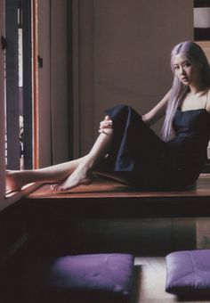 a woman sitting on top of a wooden table next to a purple pillow and window