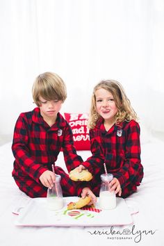 two young children sitting on top of a bed with food and drinks in front of them