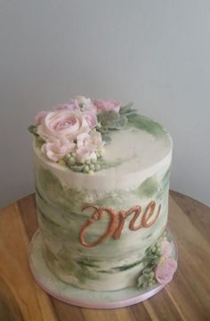 there is a cake that has flowers on it and the words one are spelled in cursive letters