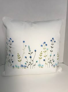 a white pillow with blue flowers and green leaves on it sitting next to a wall