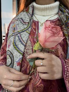 a woman is holding a pink rose in her right hand and wearing a white ring