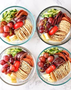 four bowls filled with crackers, grapes and cheese on top of a marble counter