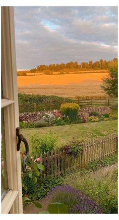 an open window looking out onto a garden and field in the distance with trees, shrubs, and flowers